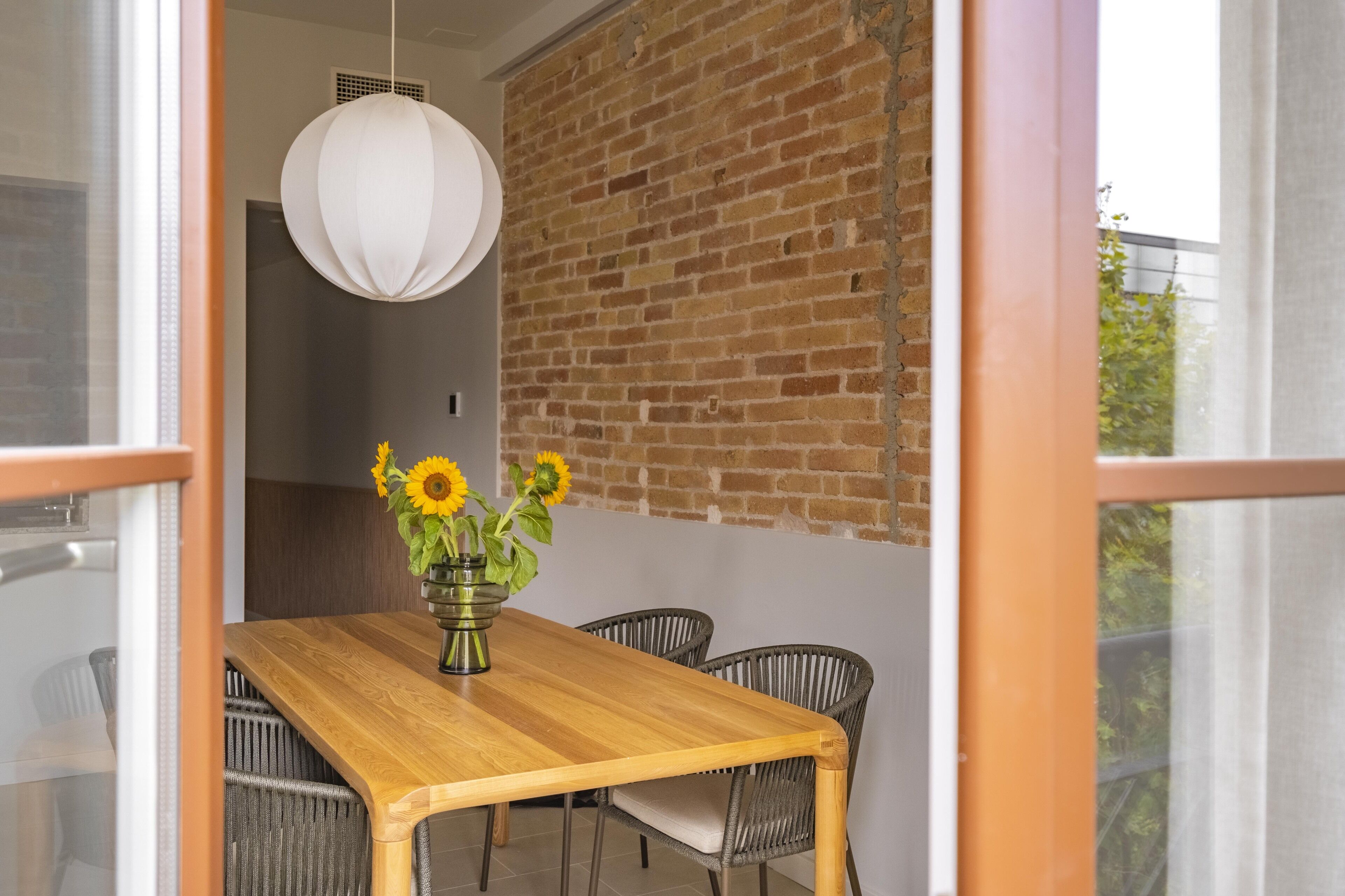Un comedor con una mesa de madera, cuatro sillas de mimbre y un jarrón con girasoles.