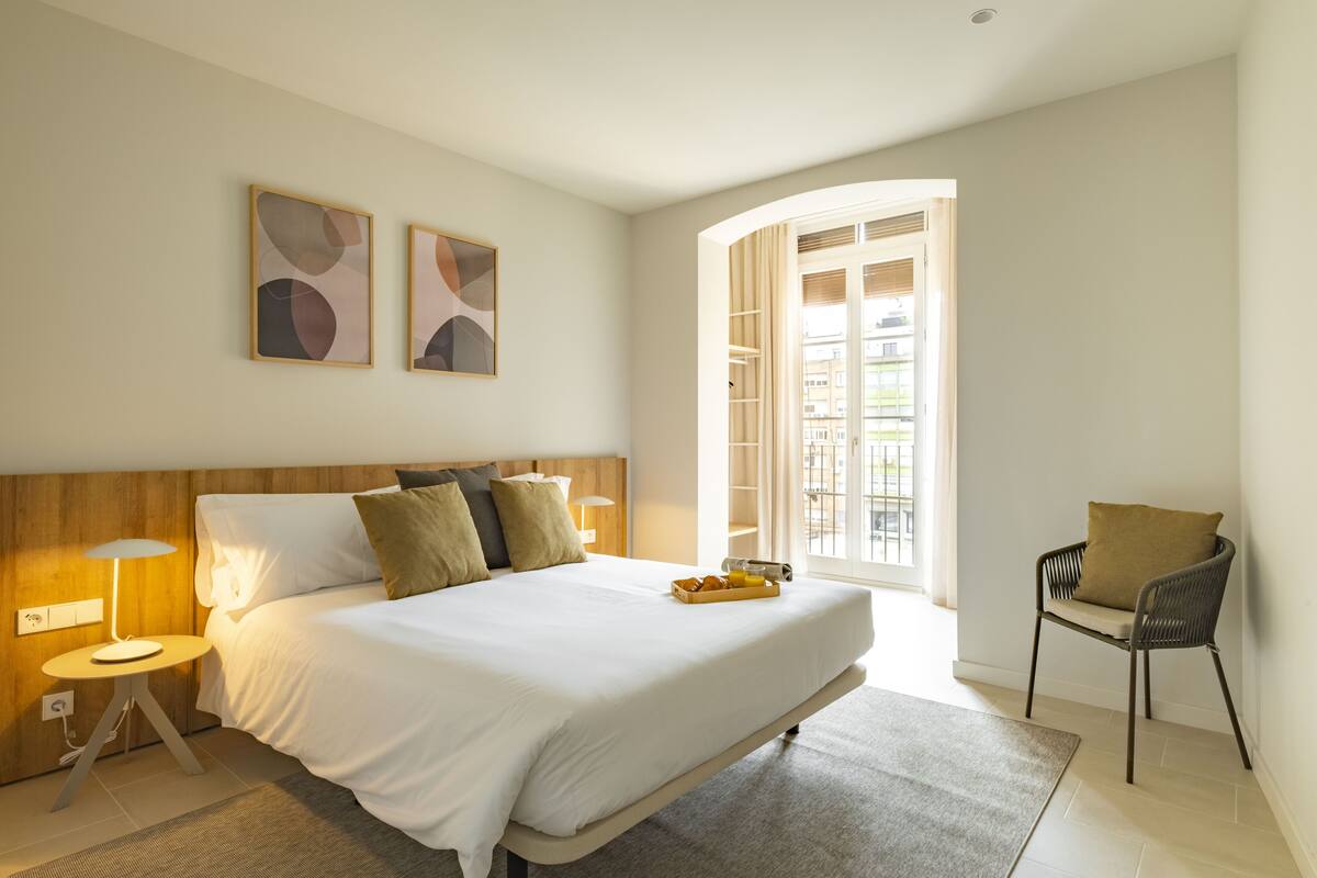 A modern hotel room with a large bed, bedside lamps, a chair, and artwork on the walls.
