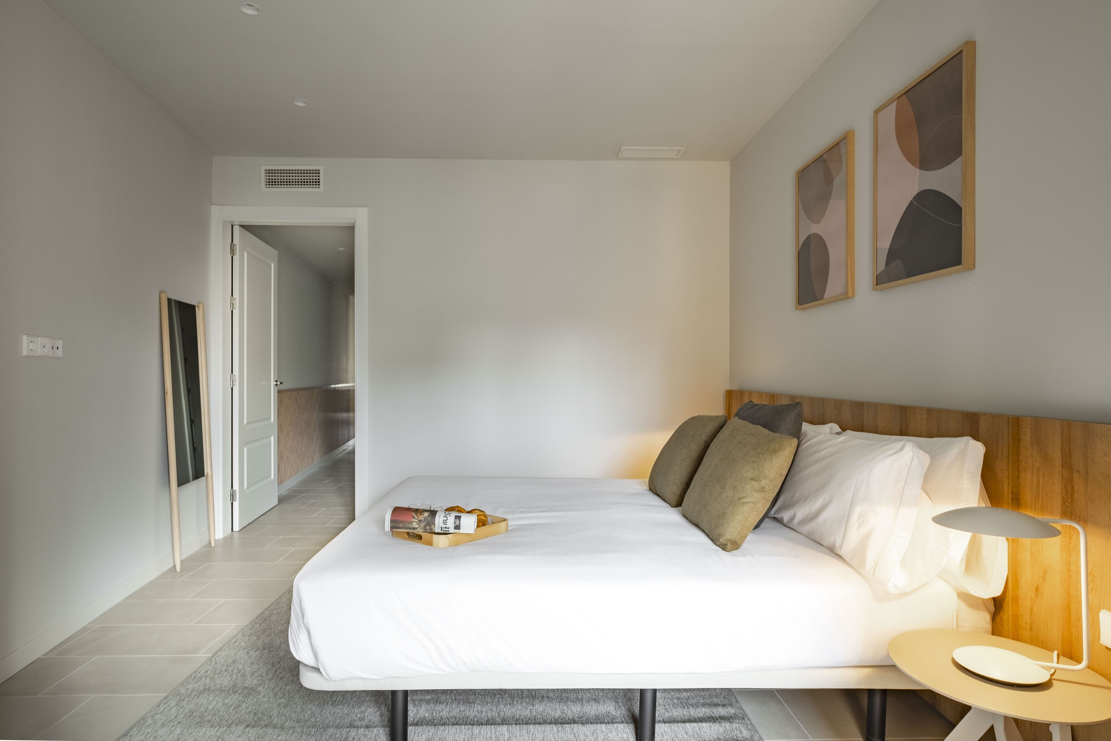 Ein modernes Hotelzimmer mit einem großen Bett, einem Nachttisch mit Lampe und abstrakter Wandkunst.