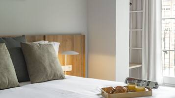 Een opgemaakt bed met kussens, een schaal met croissants en sap, en een krant.
