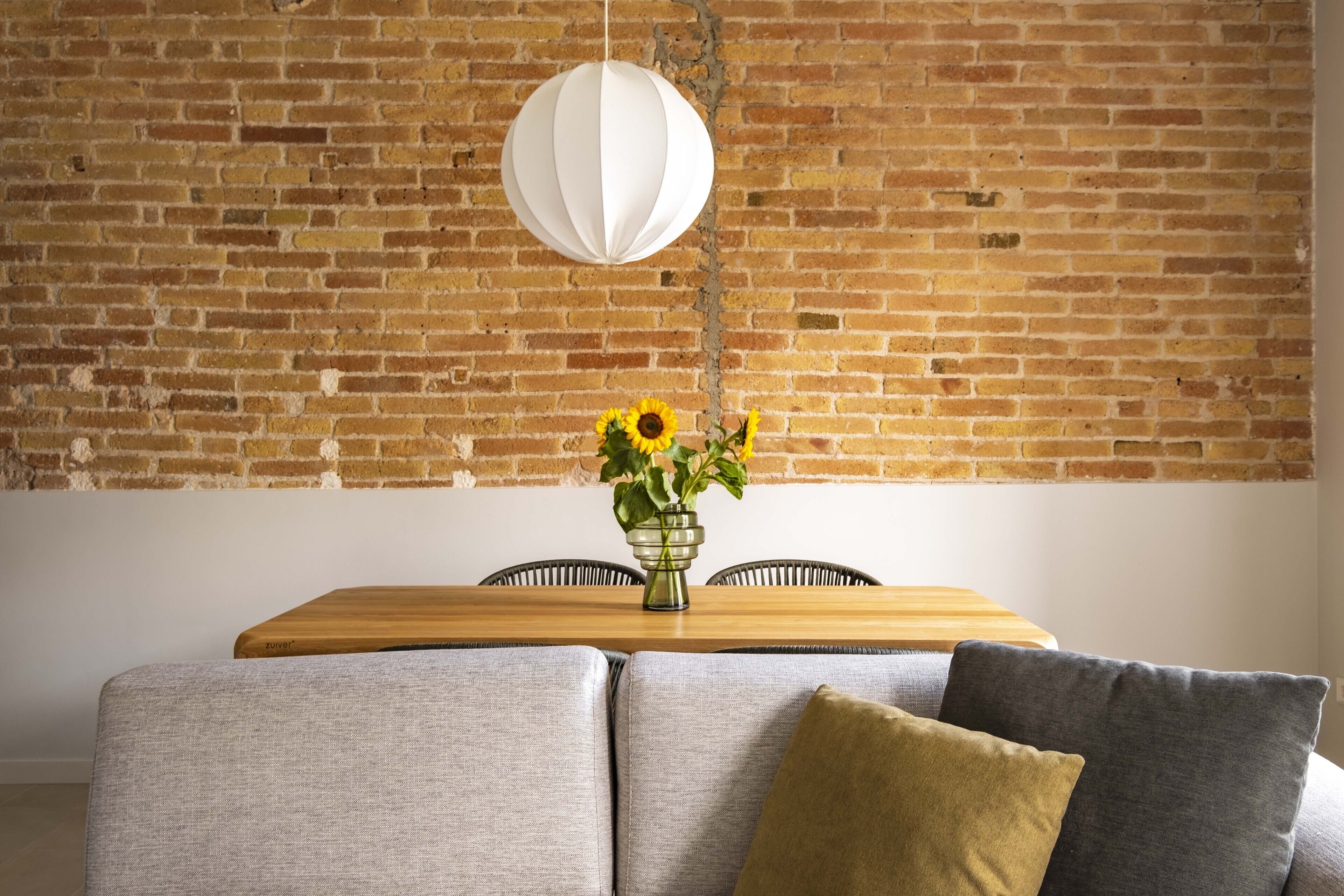 A dining area with a brick wall, a wooden table, and a vase with sunflowers.