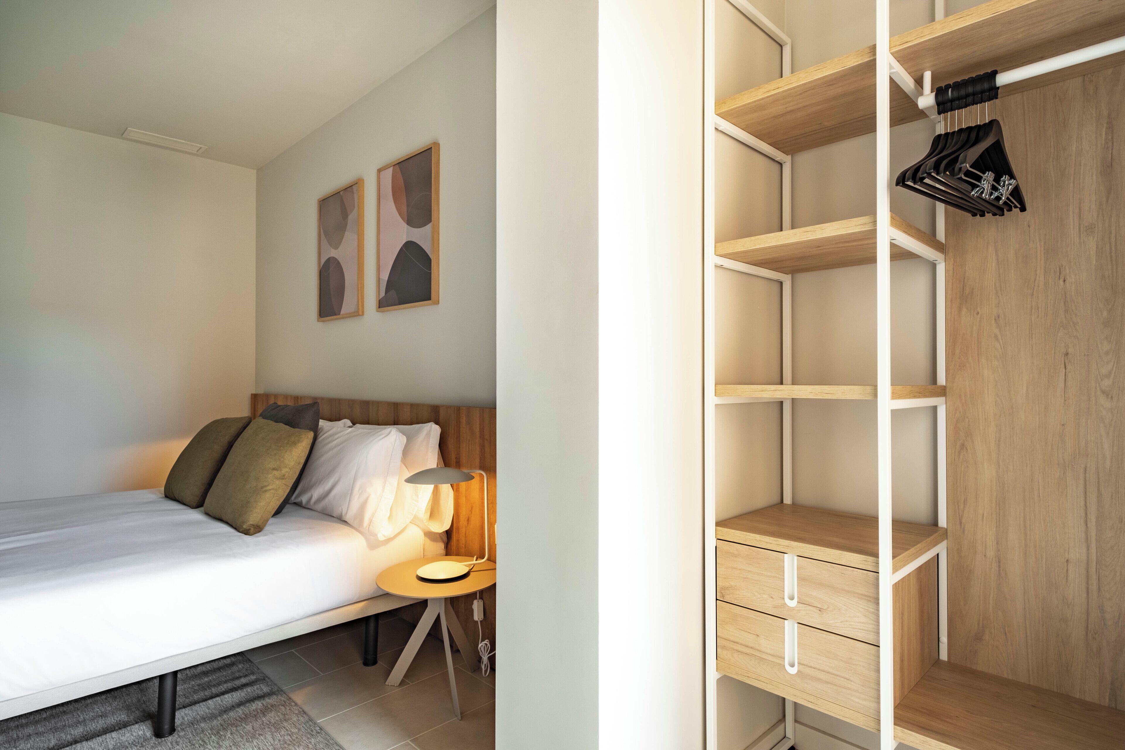 A bedroom with a bed, bedside table, lamp, and a wooden wardrobe with hanging space.