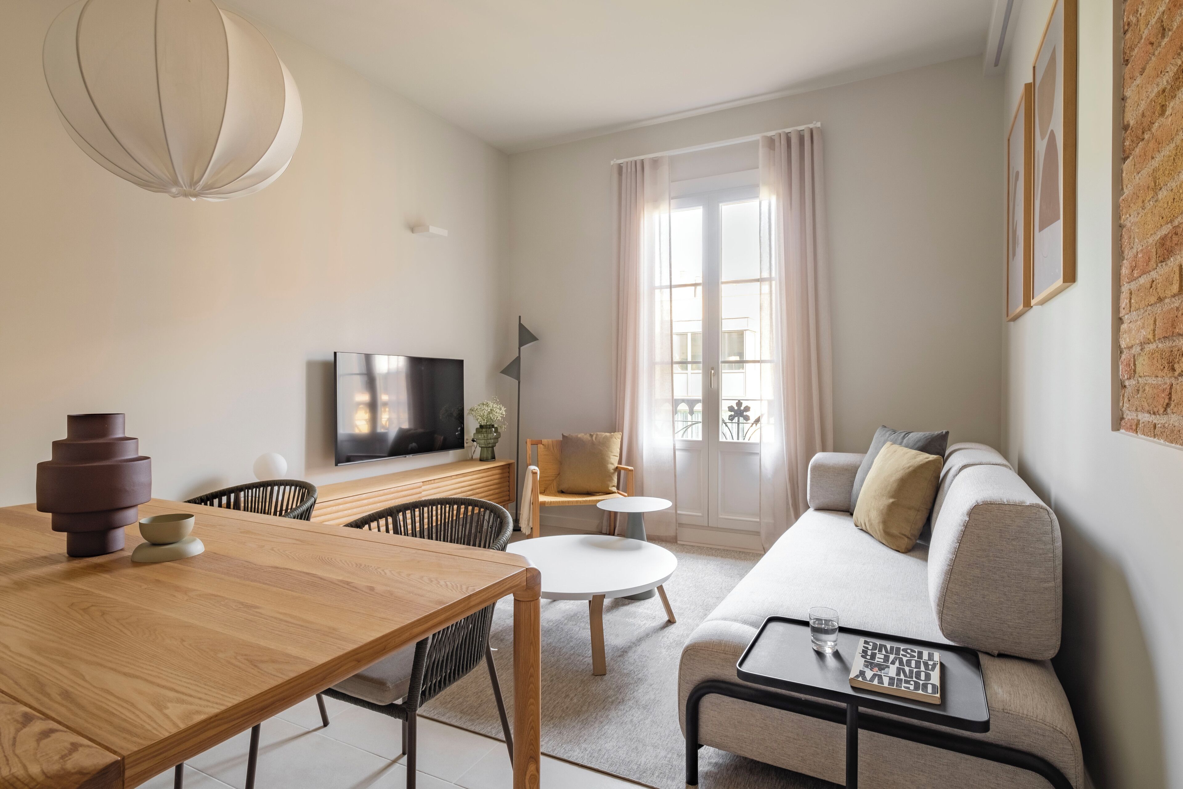 Ein modernes Wohnzimmer mit einem Holzesstisch, einer Couch, einem Fernseher und einem großen Fenster mit Vorhängen.