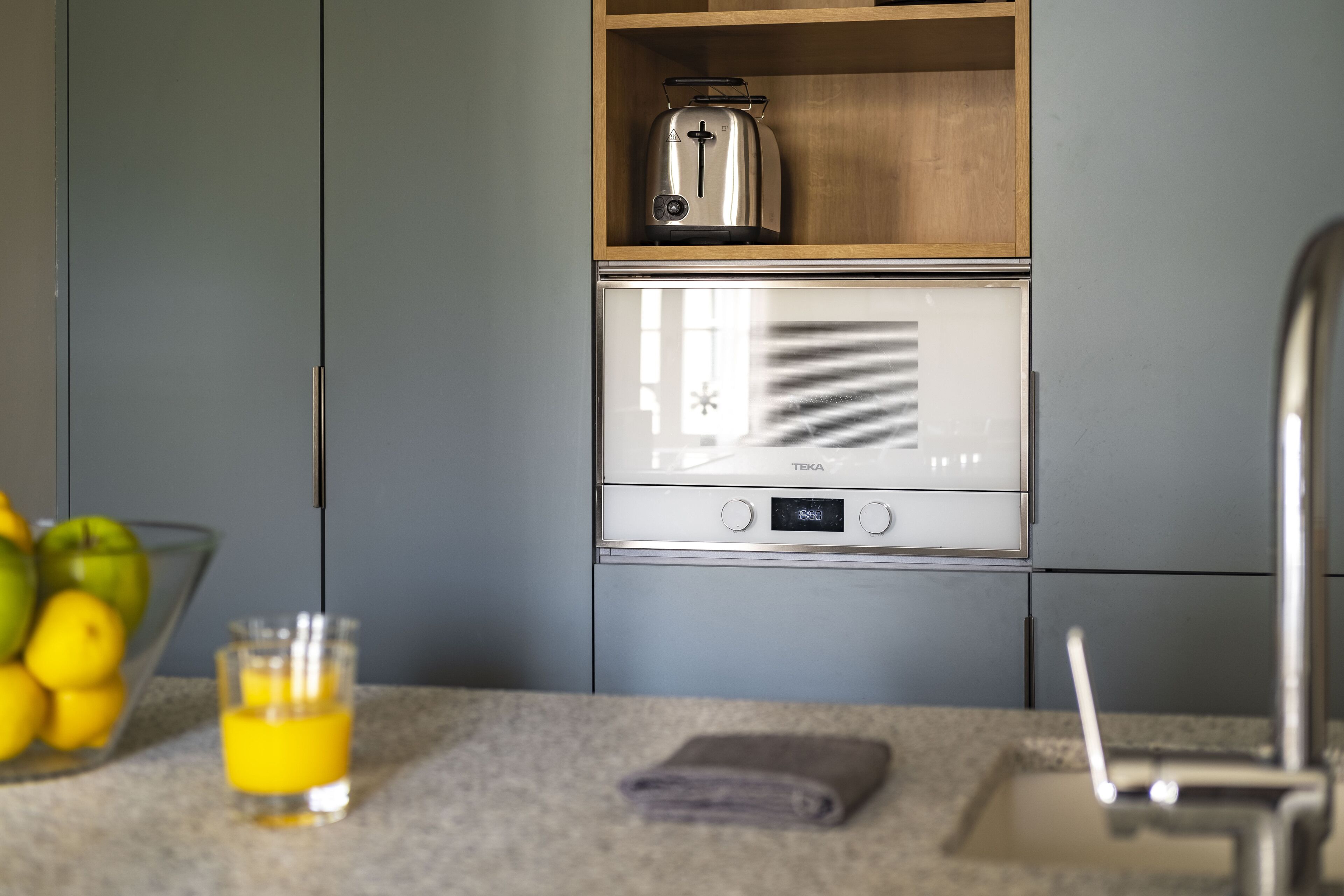 Une cuisine équipée d’un four à micro-ondes, d’un grille-pain et d’un saladier rempli de fruits, posé sur le comptoir.