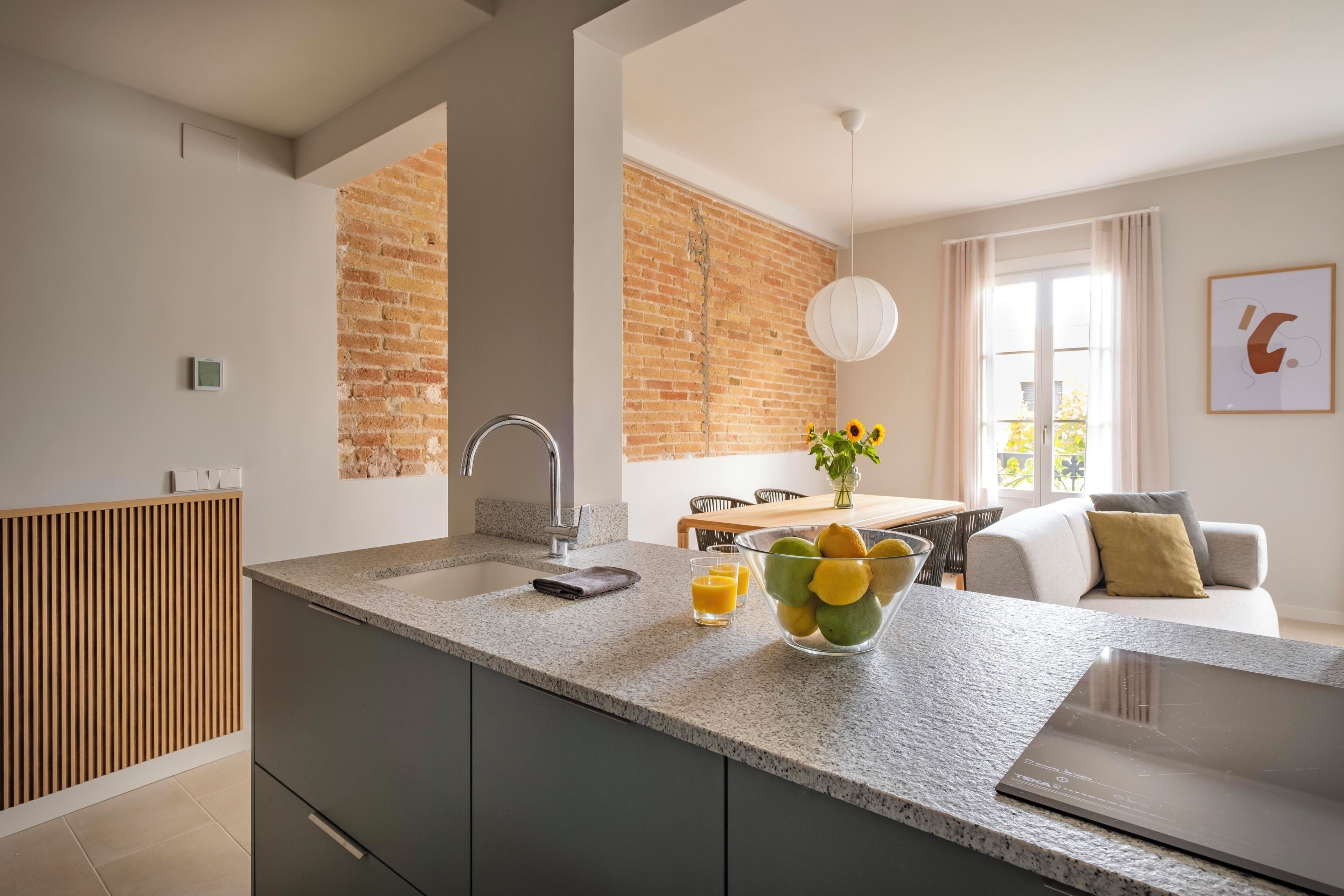 A modern kitchen with a granite countertop, a built-in oven, and a brick wall.