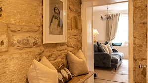 Ein Zimmer mit Steinwänden, einer Bank, einem gerahmten Bild, einem dunklen Sofa und einer Chandelier.