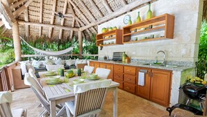 Una cocina exterior con armarios de madera, una parrilla y una zona de comedor con mesa y sillas.