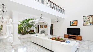 Amplia sala de estar con un sofá blanco, un televisor y un balcón con barandilla.
