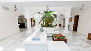 Un vestíbulo amplio con un sofá blanco, una mesa de centro con flores y una planta grande.
