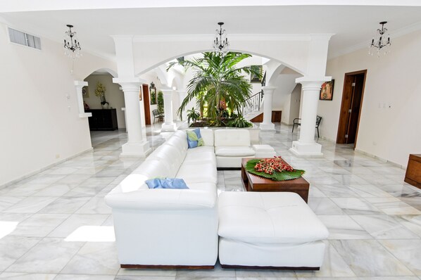 A spacious lobby with a white sofa, a coffee table with flowers, and a large plant.