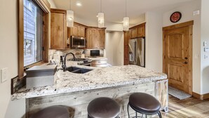 A modern kitchen with wooden cabinets, granite countertops, stainless steel appliances, and pendant lighting. - Luxury 2 Bedroom Townhome Close to Main Street!! (Frisco)