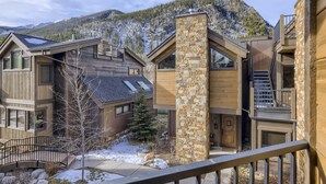 A modern multi-story building with a stone facade, wooden exterior, and a balcony overlooking a snowy mountain. - Luxury 2 Bedroom Townhome Close to Main Street!! (Frisco)
