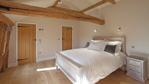 Une chambre avec un plafond en bois, un lit avec une literie blanche, deux portes et une table de chevet avec des tiroirs.