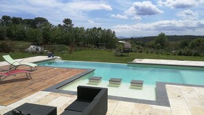 Une piscine dotée d’une terrasse en bois et de chaises longues, entourée d’une pelouse et d’arbres.