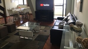 A modern living room with a glass coffee table, a black leather sofa, a flat-screen TV, and a dining area with a white table and chairs. - Spectacular Triplex Penthouse on Morro Beach (ES)