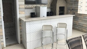 A kitchen area with a tiled backsplash, a flat-screen TV, a built-in oven, and two bar stools. - Spectacular Triplex Penthouse on Morro Beach (ES)