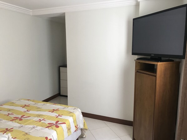 A hotel room with a bed, a television on a wooden stand, and a wardrobe.