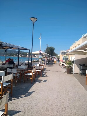 A seaside promenade with outdoor seating, a no parking sign, and a clear view of the sea.