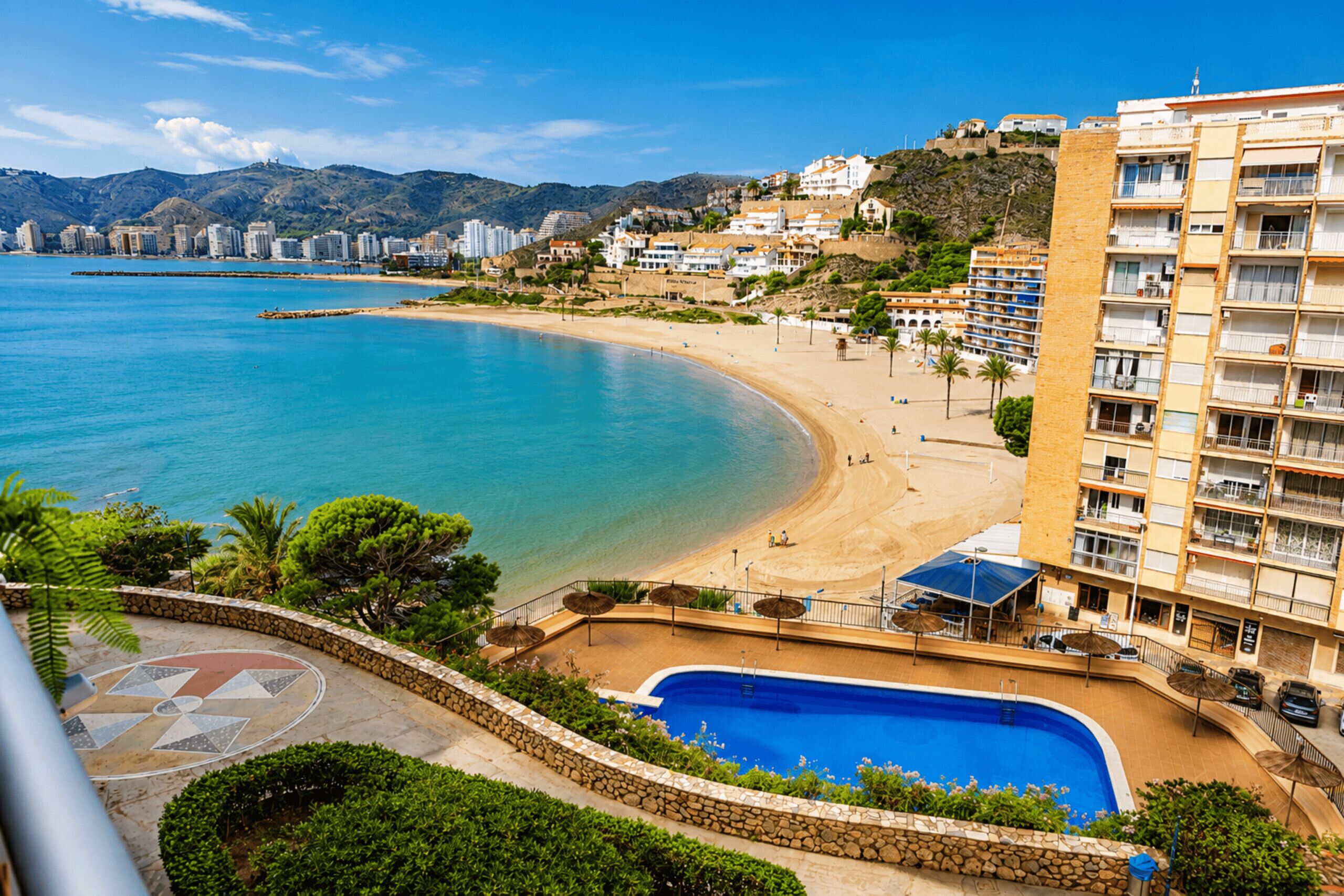 A coastal hotel with a pool, beach, and mountain backdrop.