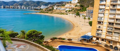A coastal hotel with a pool, beach, and mountain backdrop.