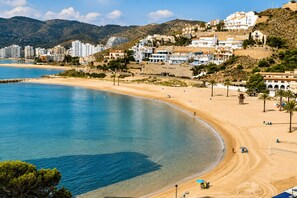 Un pueblo costero con playa de arena, aguas azules cristalinas y edificios en una ladera.