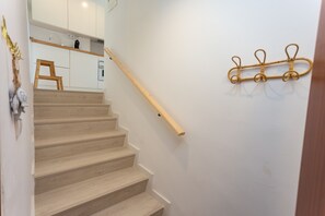 Eine Treppe mit Holzbeschlägen und Handlauf, die zu einer Küche mit weißen Schränken und einem Holzregal führt.