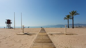 A wooden boardwalk leading to a lifeguard tower and palm trees on a beach.