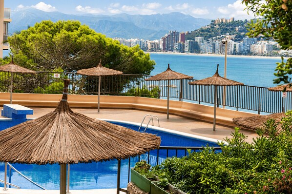 A pool area with a view of the sea and a cityscape in the background.