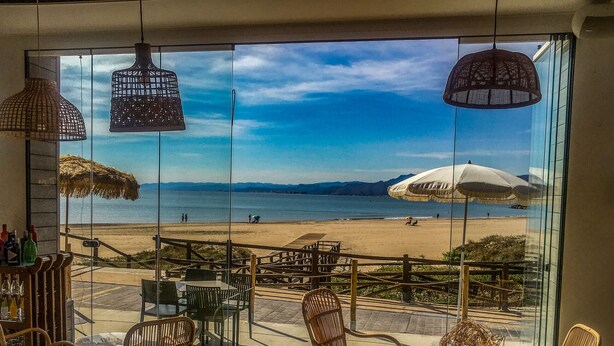 A beachside terrace with wicker furniture, a bar area, and a view of the beach and ocean.