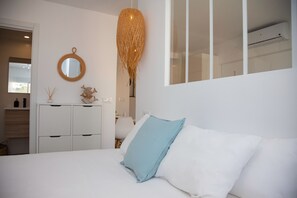 Una camera da letto con un letto, pareti bianche, uno specchio, una lampada a sospensione e una finestra.