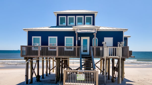 Une maison de plage à l’extérieur bleu, dotée de nombreuses fenêtres et d’une terrasse en bois.