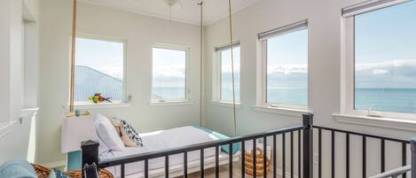 A bright, airy bedroom with a bed, a crib, and large windows offering ocean views.