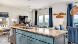 Une cuisine moderne dotée d’un grand îlot central, de meubles bleus et offrant une vue sur l’océan.