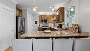 Una cocina con encimeras de granito, armarios de madera, un refrigerador de acero inoxidable e iluminación colgante.