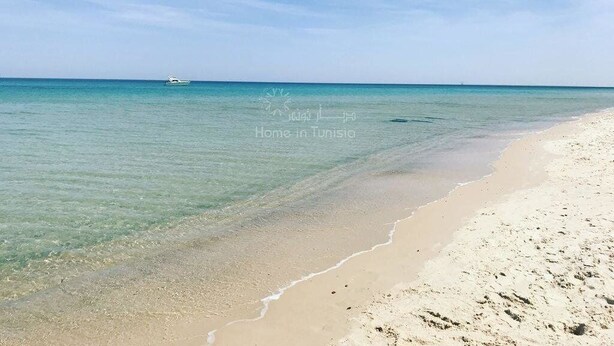 A beach with clear turquoise water, a boat in the distance, and a sandy shore. - Superb studio for vaccinations (Sousse)