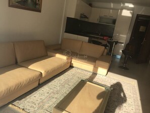 A living room with a beige sofa, a patterned rug, and a kitchen in the background.