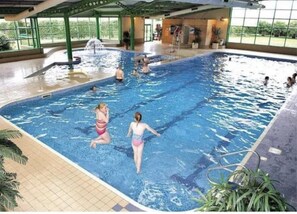 Una piscina interior con agua cristalina, suelo de baldosas y estructura de techo verde.