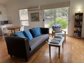 Un salon comprenant un canapé en cuir foncé, une table basse en bois, une bibliothèque et un coin repas avec une table et des chaises.