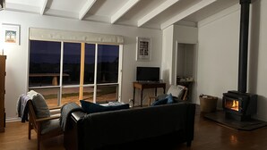 Ein Wohnzimmer mit einer Couch, einem Fernseher, einem Kamin und großen Fenstern.