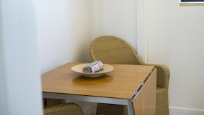 Une petite table en bois, une chaise en osier, un objet enroulé posé sur la table et une fenêtre en arrière-plan.