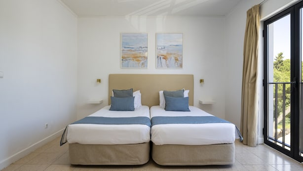 Une chambre double avec deux lits, une grande fenêtre avec des rideaux et deux tableaux accrochés au mur.