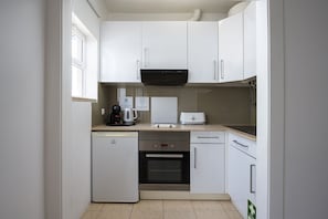 A compact kitchen with white cabinets, a built-in oven, a coffee maker, and a toaster.