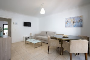 A modern living room with a sofa, coffee table, dining table with chairs, a flat-screen TV, and artwork on the wall.