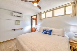 Une chambre à coucher comprenant un lit, un ventilateur de plafond, une fenêtre avec des rideaux, une lampe de chevet et un climatiseur fixé au mur.