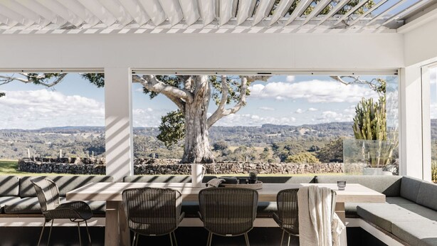 A modern outdoor dining area with a stone wall, wicker chairs, and a view of a tree and landscape. - Amileka - luxury 25 acre estate with pool (Federal)