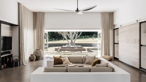 A modern living room with a large sofa, a flat-screen TV, and a ceiling fan. - Amileka - luxury 25 acre estate with pool (Federal)