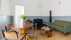 A room with a round wooden table surrounded by wicker chairs, a blue sofa, and a patterned green sofa.