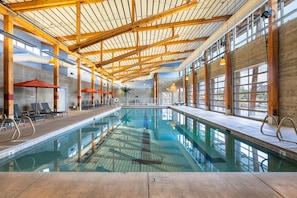 Ein Innenpool mit Holzbalken, Liegestühlen und großen Fenstern.
