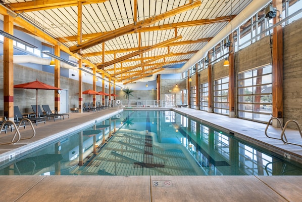 An indoor swimming pool with wooden beams, lounge chairs, and large windows.