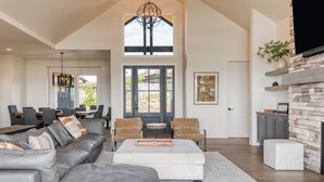 Een ruime woonkamer met een grote hoekbank, een witte voetenbank en een eethoek met een tafel en stoelen.
